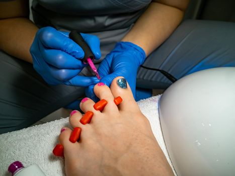 gloved master makes a pedicure for a client. close-up no face. woman in a nail salon paints her nails with varnish