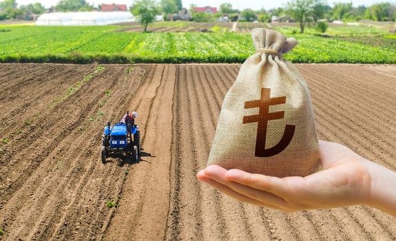 Hand with a Turkish lira money bag on the background of a farm field with a tractor. Subsidies support for agricultural producers. Land lease, land market. Investments in agriculture and agribusiness.