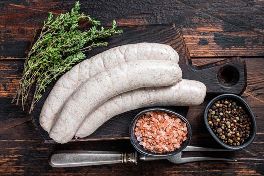 Munich traditional white sausages on a wooden board with thyme. Dark wooden background. Top view