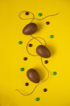 Flat lay composition with chocolate Easter eggs and chocolate sweets on yellow background. View from above, empty space for text.
