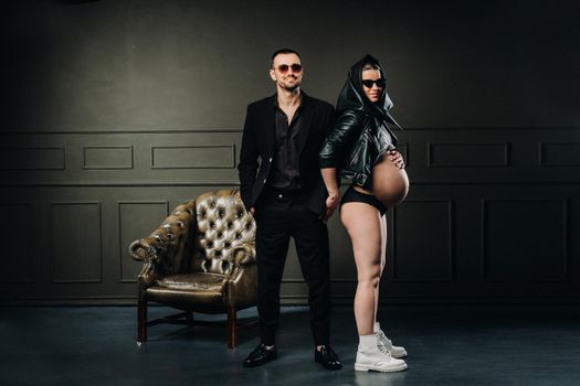 a pregnant woman in black clothes and a headscarf and a man in a suit in a studio on a dark background