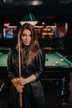 A girl with a cue in her hands is standing in a billiard club.Russian billiards