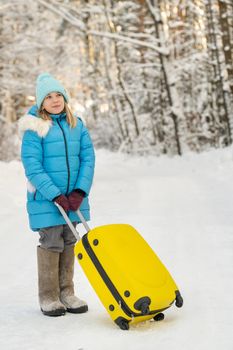 A girl in winter in felt boots goes with a suitcase on a frosty snowy day