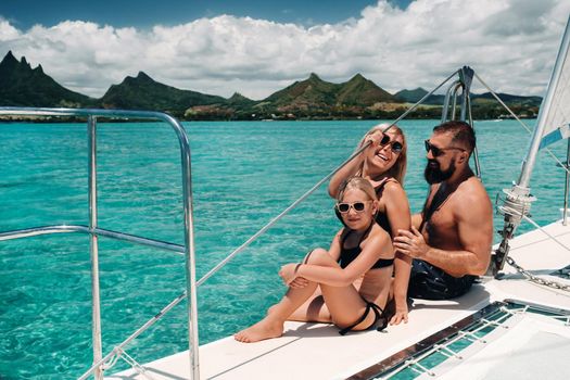 a happy family in swimsuits sits on a catamaran in the Indian ocean. portrait of a family on a yacht in the coral reef of the island of Mauritius.