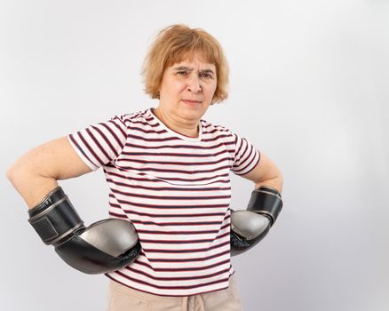 Elderly woman in fighting gloves in a defensive pose on a white background.