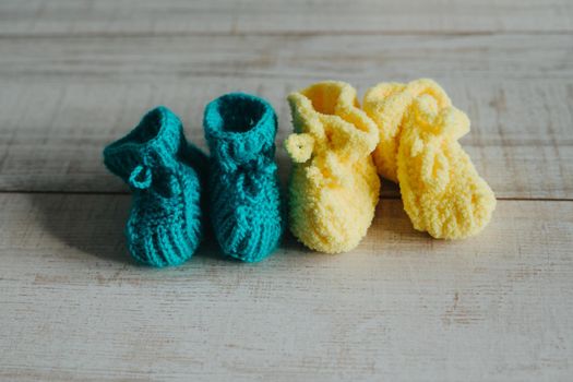 Yellow and mint knitted booties on the wooden floor.