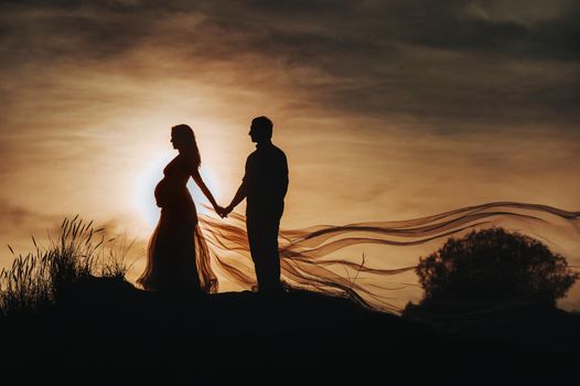 Silhouette of a couple Pregnant couple hug and holding belly talking with their child on sunset background.