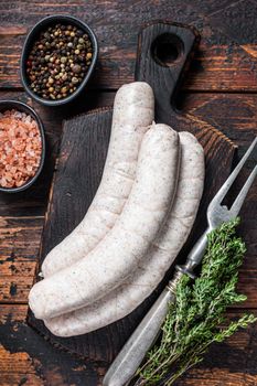 Munich traditional white sausages on a wooden board with thyme. Dark wooden background. Top view
