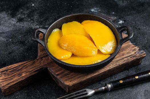 Canned mango slices in bowl. Black background. Top view