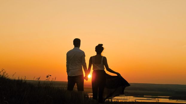 Young loving couple - brave man and beautiful girl at dusk silhouette, looking to sun
