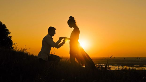 Romantic Silhouette of Man Getting Down on his Knee and Proposing to Woman high hill - Couple Gets Engaged at Sunset - Putting Ring Girl's Finger, slow motion