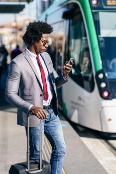 Black Businessman wearing suit waiting his train on an outdoors station. Man with afro hair.