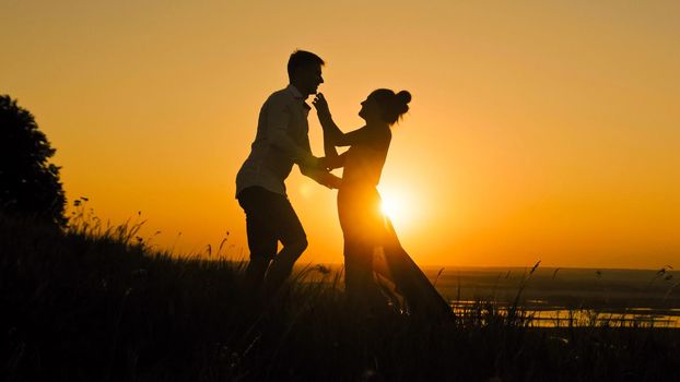 loving couple - brave young man and beautiful girl stands on high hill at sunset have hugs kiss, silhouette, slider shot