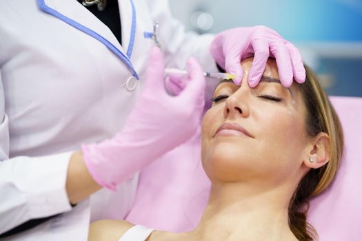 Aesthetic doctor injecting botulinum toxin into the forehead of her middle-aged patient.