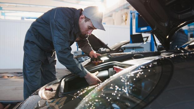 Mechanic male in automobile garage checking hood of luxury sportcar