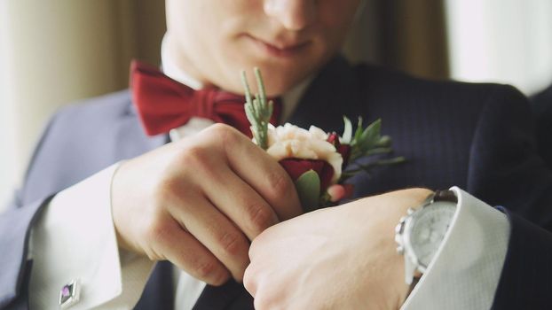 Fashion young man in bow tie and clock - groom's hand arranging boutonniere flower on suit