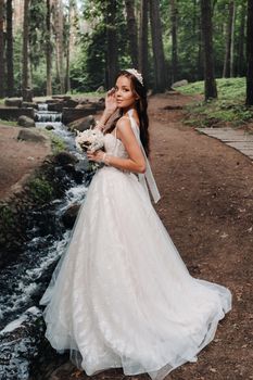 An elegant bride in a white dress and gloves holding a bouquet stands by a stream in the forest, enjoying nature.A model in a wedding dress and gloves in a nature Park.Belarus