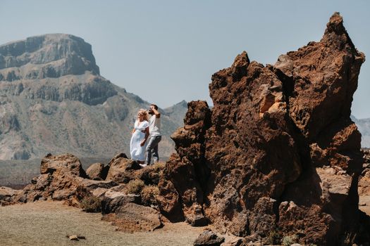 a guy and a girl in white clothes and glasses stand in the crater of the El Teide volcano, a Couple stands on a mountain in the crater of a volcano on the island of Tenerife, Spain