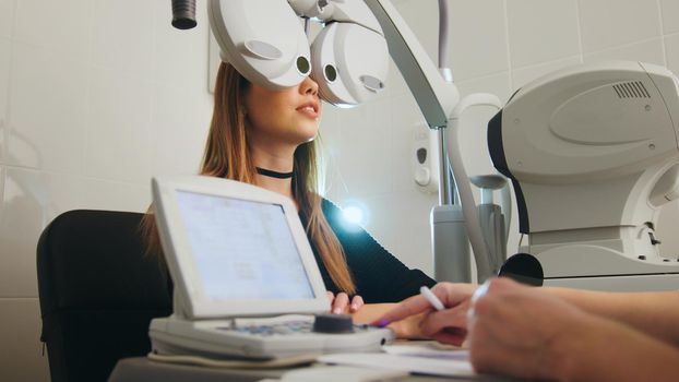 Blonde young female doing eye test with optometrist in medical center