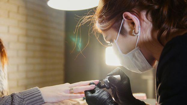 Manual labour - professional manicurist - nail master in medical mask doing professional manicure, close up