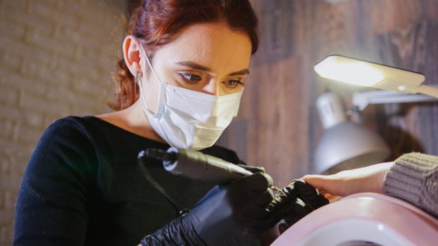 Woman manicurist in medical mask doing manicure in beauty salon