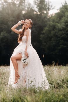 On the wedding day, an Elegant bride in a white long dress and gloves with a bouquet in her hands stands in a clearing enjoying nature. Belarus.