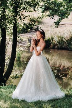 An elegant bride in a white dress, gloves with a bouquet on a waterfall in the Park, enjoying nature.Model in a wedding dress and gloves in the forest.Belarus