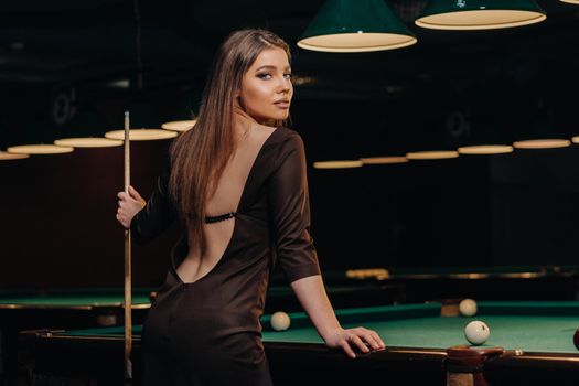 A girl in a hat in a billiard club with a cue in her hands.Pool Game
