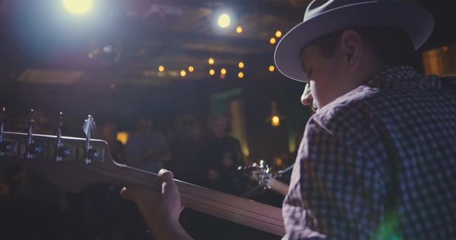 Musician - guitarist in hat plays guitar in night club, rear view