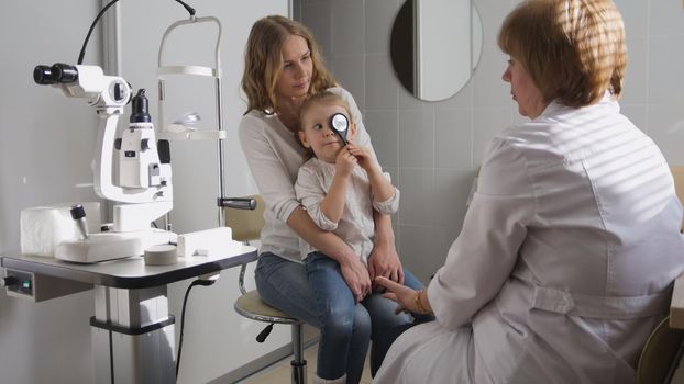 Ophthalmologist in clinic explains diagnosis about girl's eyesight - child plays