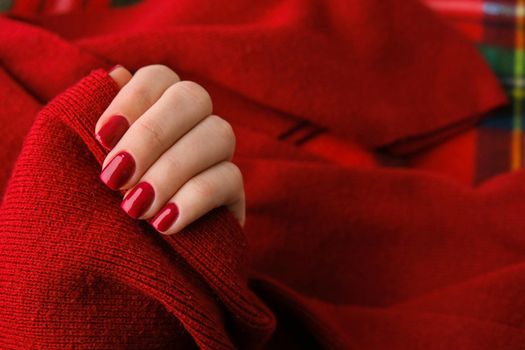 Woman manicured hands, stylish red nails, copy space. Red sweater Closeup. Winter or autumn style of nail design concept. Beauty treatment