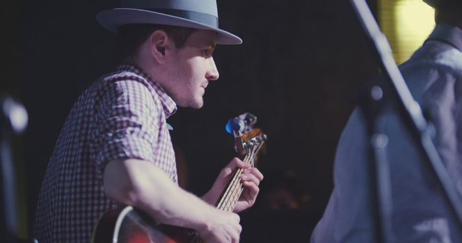 Musician in hat plays guitar in night club, close up