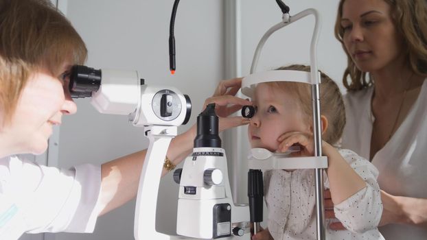 Optometrist checks little girl's eyesight - mother and child in ophthalmologist room