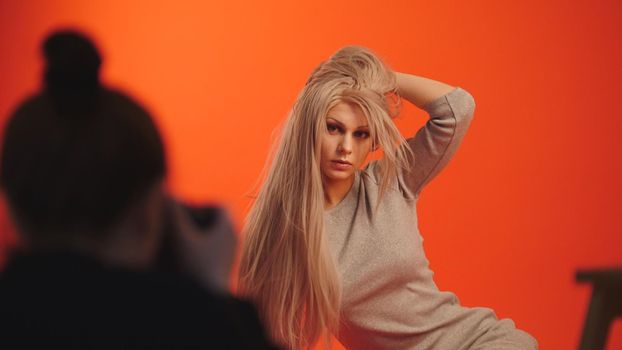 Backstage: blonde female model posing for photographer in red studio