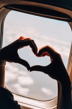 Female hand in heart shape View from the window of the plane. Airplane, Aircraft. Traveling by air. Vacation love travel concept Airplane Window View Above the Clouds Amazing golden fluffy clouds moving softly