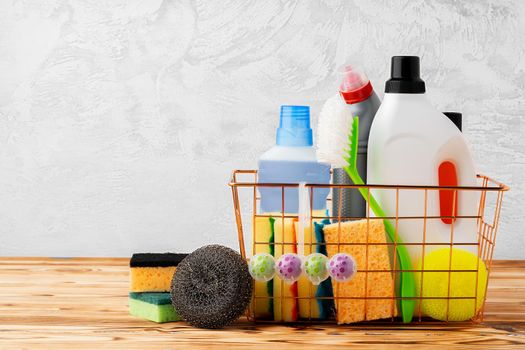 Cleaning tools and chemicals in basket on wooden table against gray background