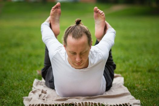 A man - yoga instructor performs flexibility exercises in park