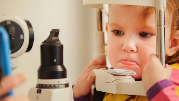 Child's optometry concept - little girl angry when checks eyesight in eye ophthalmological clinic, telephoto