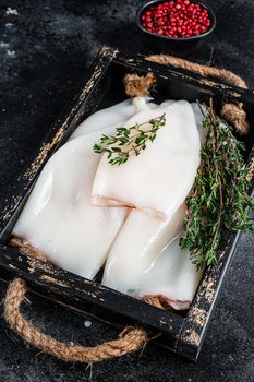 Raw white Squid or Calamari in a wooden tray with herbs. Black background. Top view