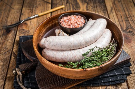 Raw Munich traditional white sausages in a wooden plate with herbs. wooden background. Top view