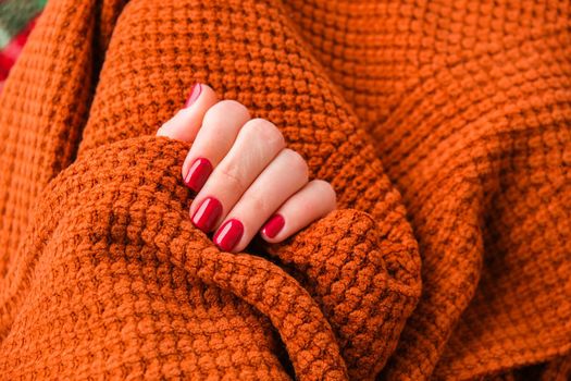 Woman manicured hands, stylish red nails, copy space. Orange sweater Closeup. Winter or autumn style of nail design concept. Beauty treatment