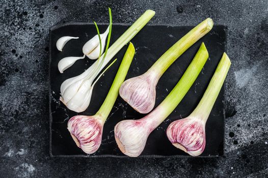 Raw Spring young garlic bulbs and cloves on marble board. Black background. Top view