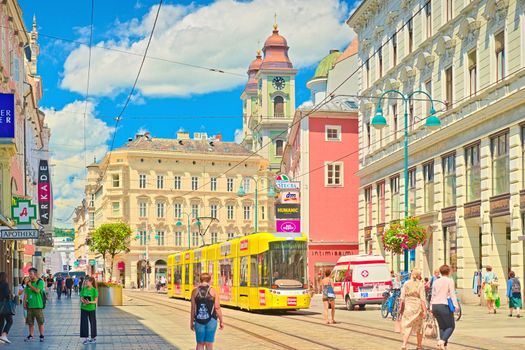 Linz - June 2020, Austria: view of the main street with walking people, yellow tram, and old colorful historical buildings