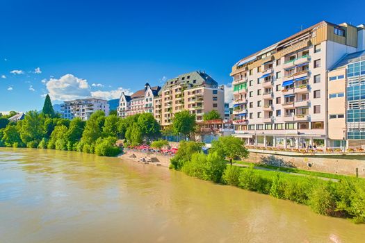 Villach- July 2020, Austria: Cityscape of a small alpine town. View of the promenade with hotel buildings, restaurants and people walking along the Drau River