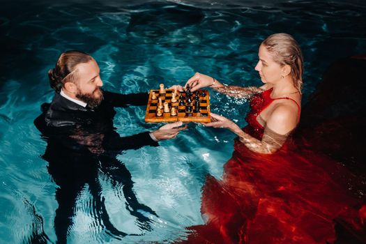 a man in a suit and a girl in a red dress play chess on the water in the pool
