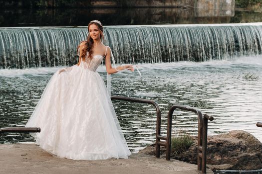An elegant bride in a white dress and gloves stands by the river in the Park, enjoying nature.A model in a wedding dress and gloves in a nature Park.Belarus
