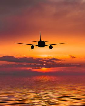 The plane flies over the sea at sunset