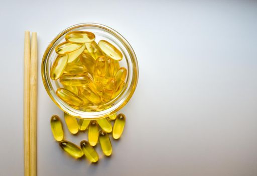 Fish oil capsules on a saucer with chopsticks. Bunch of vitamin omega 3 pills on a white background. Close-up, top view, high resolution product. Metabolism in the body. Body calcium.