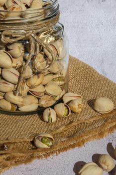 Pistachios in glass jar on concrete background. Organic pistachios, healthy food. Heap or stack of pistachios. Vegan omega nutrition