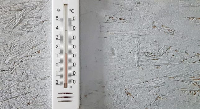 white thermometer hanging on a gray gray wooden wall indoors, background with copy space and empty place for your text